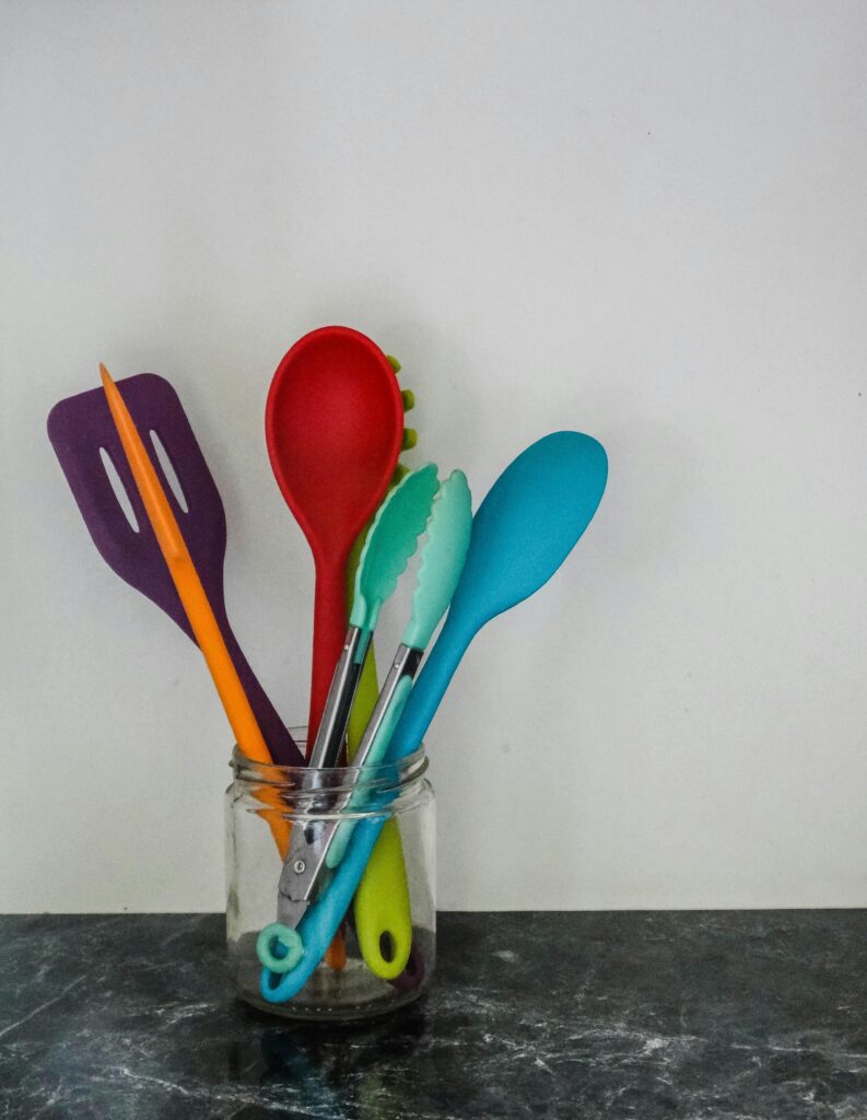 Colorful kitchen utensils in a glass jar against a neutral background.